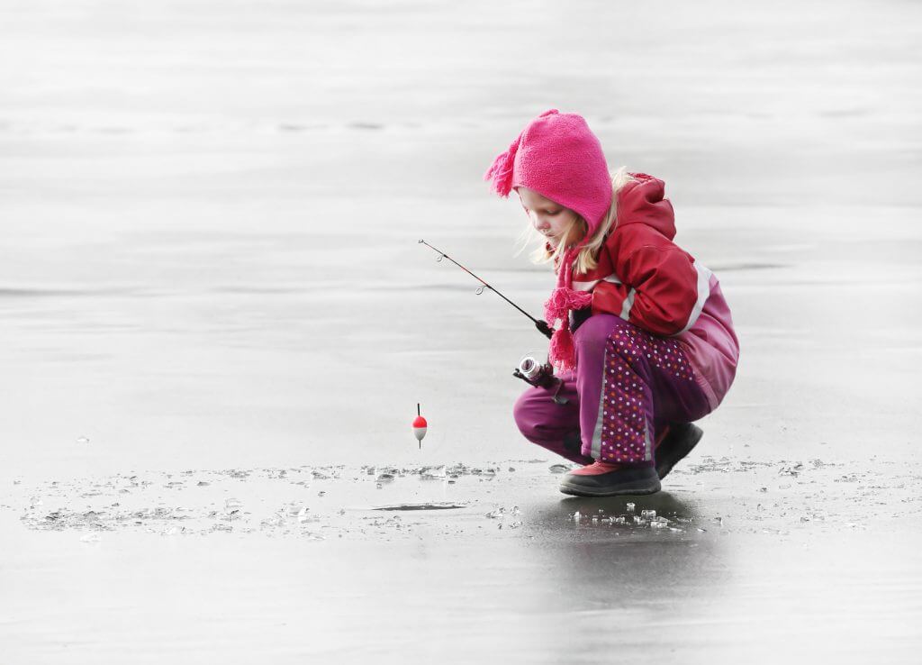 Little child fishing on a frozen lake in winter.