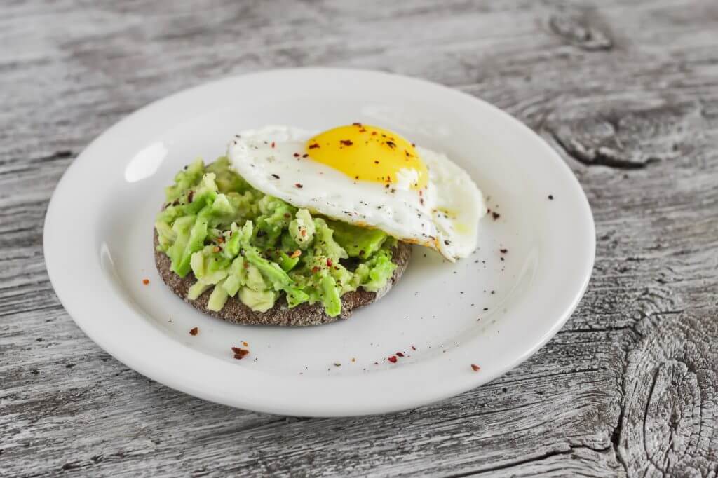 sandwich with avocado and a fried egg on a white plate on a light rustic wood surface